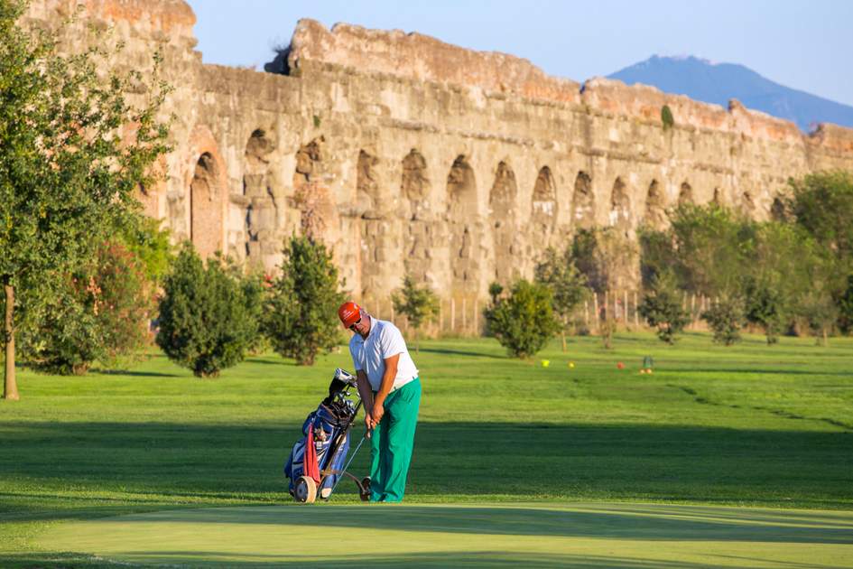 Unidentified man playing golf at the golf course next to the Ancient Roman Aqueduct in Parco degli Acquedotti. Famous Aqua Claudia Aqueduct is around 2000 years old.