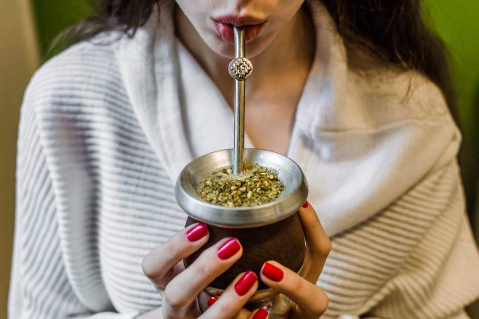 Young woman drinking traditional Argentinian yerba mate tea from a calabash gourd with bombilla stick. 