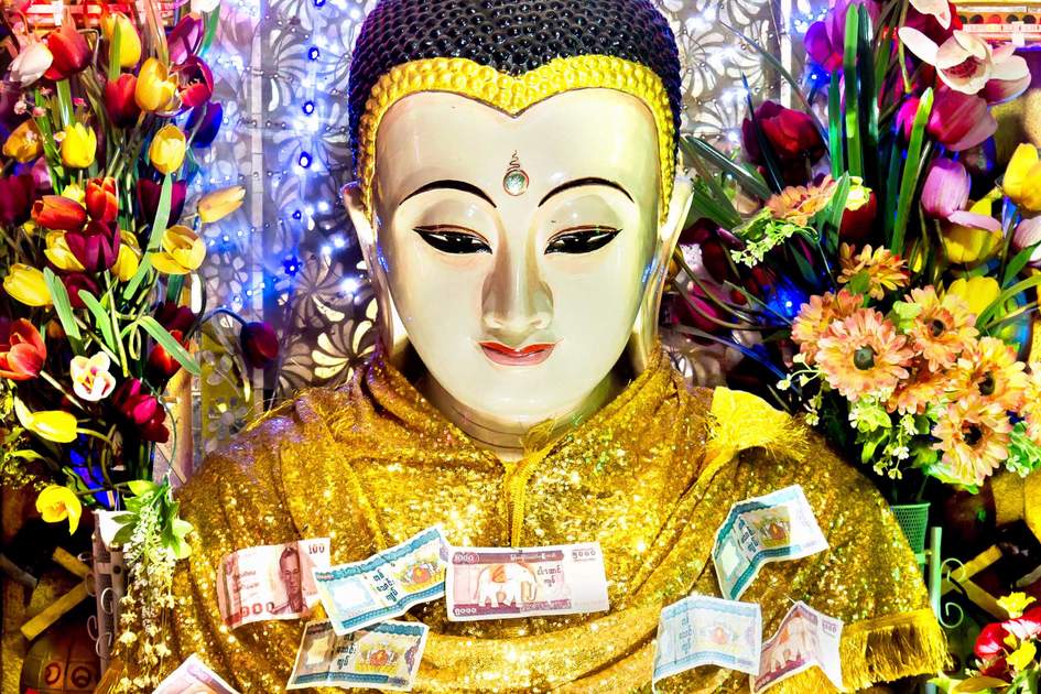 Revered Buddha statue with money and flower offerings from pilgrims at Mount Popa, Bagan, Myanmar 